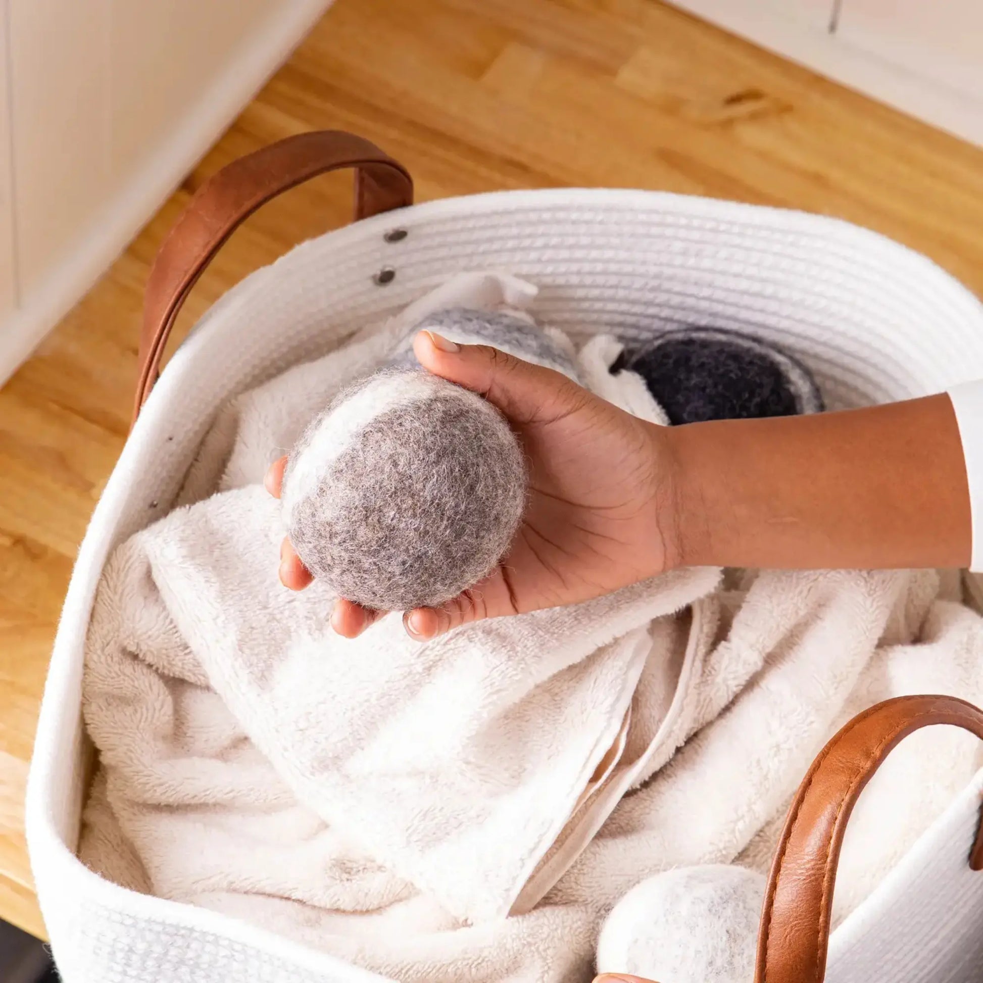 Hand holding a gray fabric ball over a basket filled with clothes on a wooden floor.