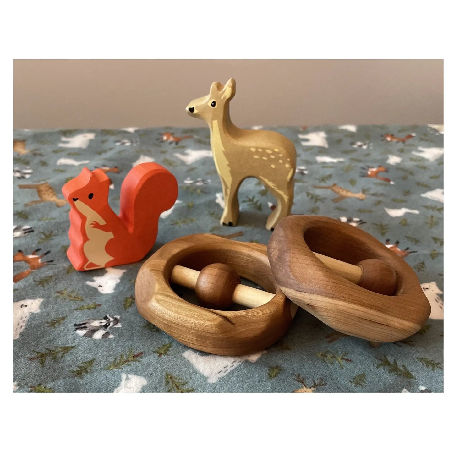 Wooden toys including a red squirrel, a deer, and two wooden cherrywood baby rattles on a patterned surface.