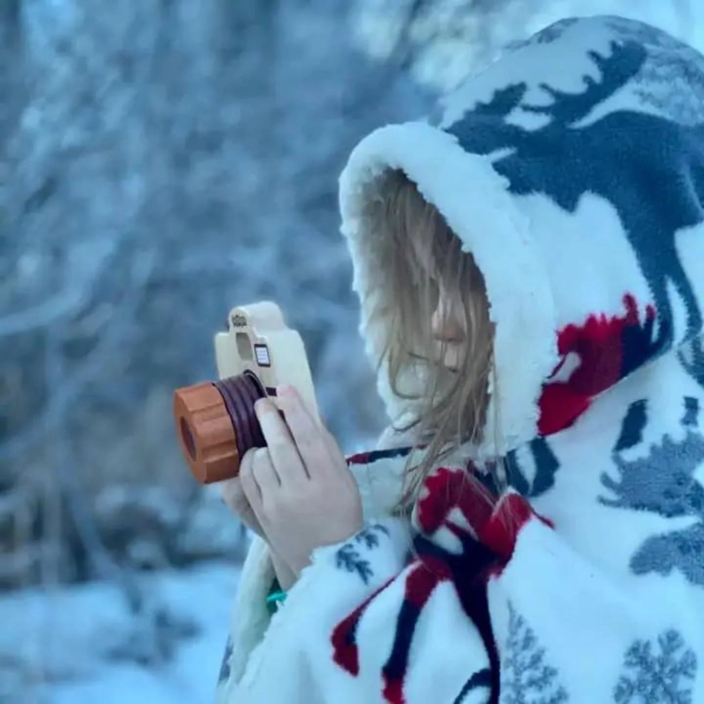 Child in a coat playing with wooden pretend play camera
