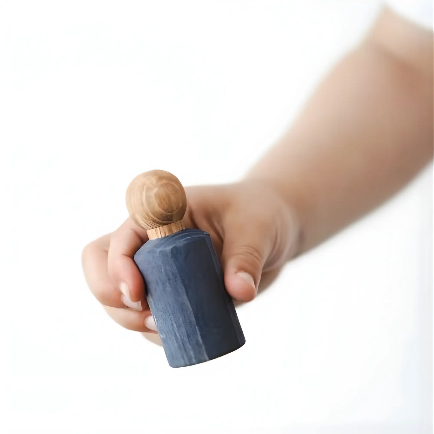 Hand holding a small blue jWaldorf inspired Blue stained peg doll against a white background