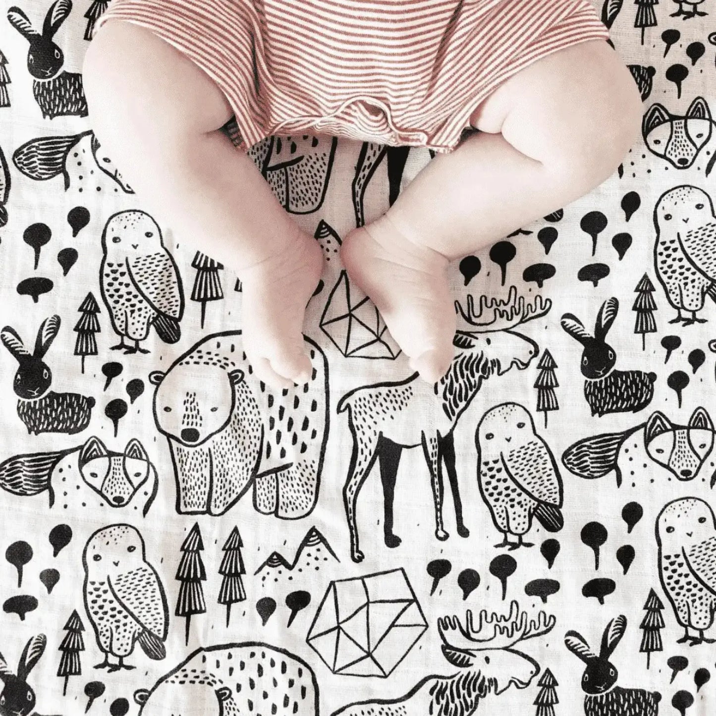 Baby legs on a organic cotton muslin cotton swaddle with black animal illustrations