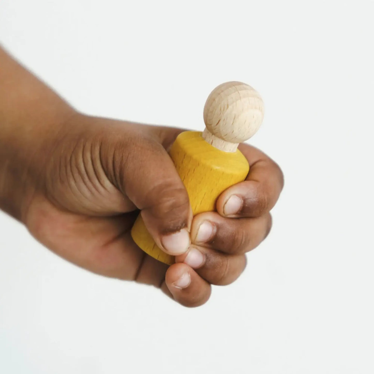 Hand holding a small blue jWaldorf inspired Yellow stained peg doll against a white background
