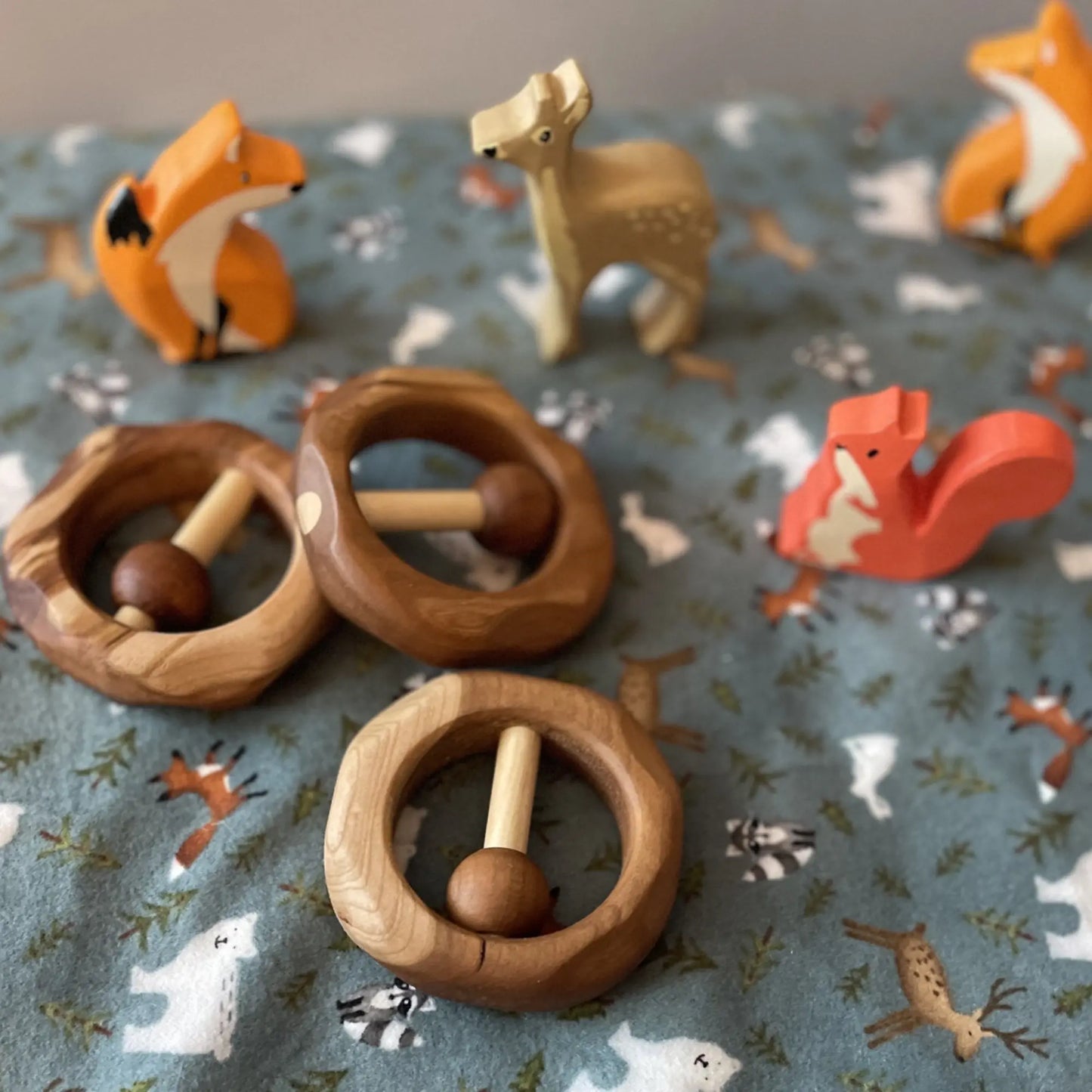Wooden animal toys and heirloom baby rattle rings on a fabric surface with animal prints