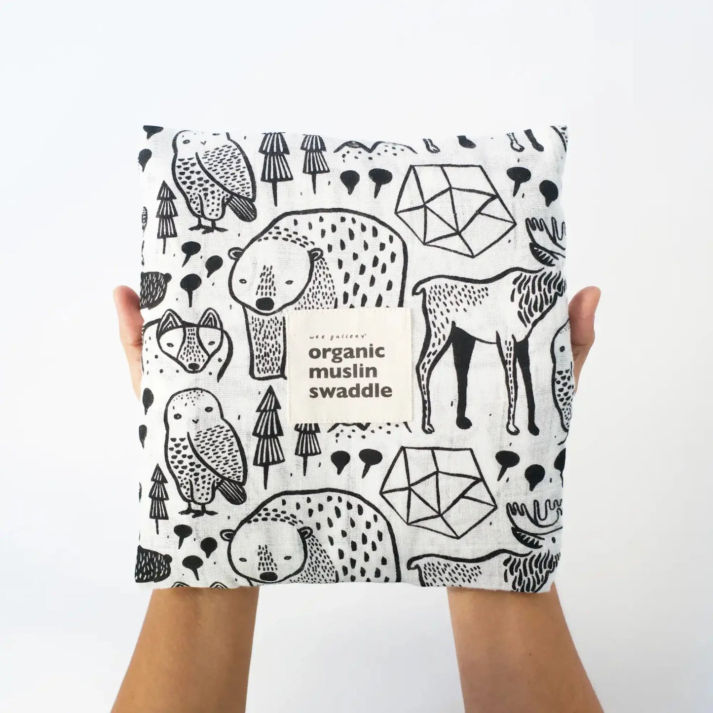 Hands Holding Organic muslin swaddle with black animal patterns on a white background