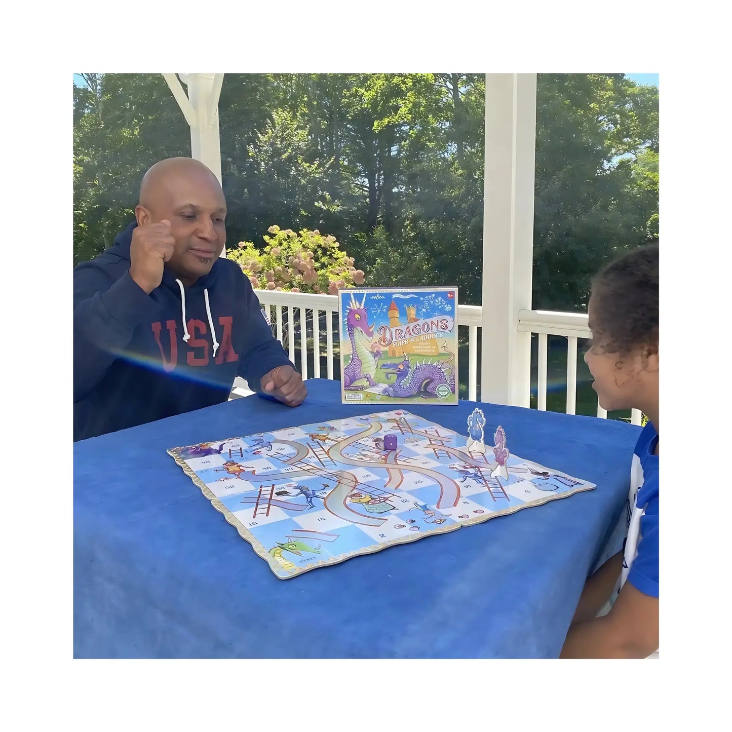 A man and preschooler playing dragons slips and ladders on a front porch