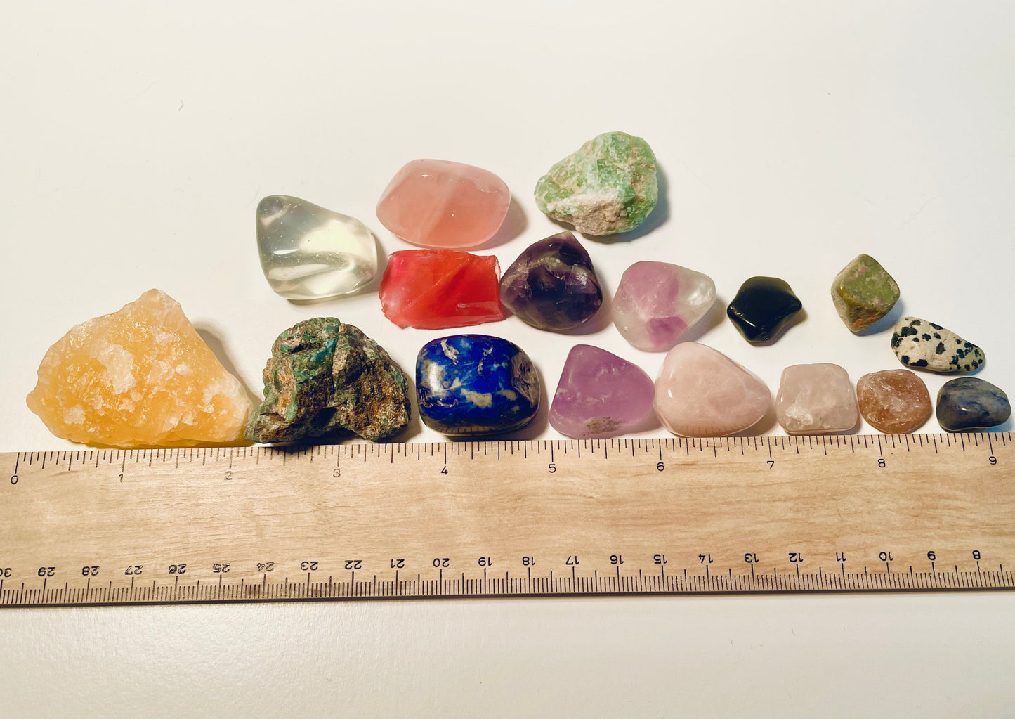 Various stones polished and raw next to a ruler to show various sizes
