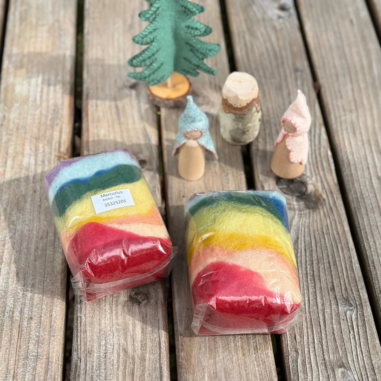 Two rainbow-colored packages on a wooden surface with small figurines in the background.