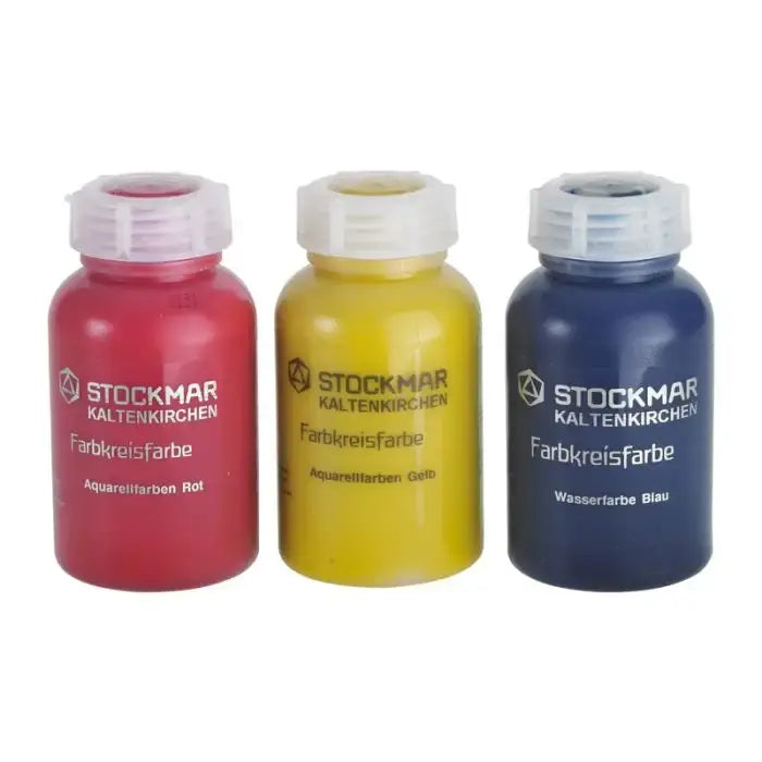 Three bottles of Stockmar watercolor paint in red, yellow, and blue on a white background.