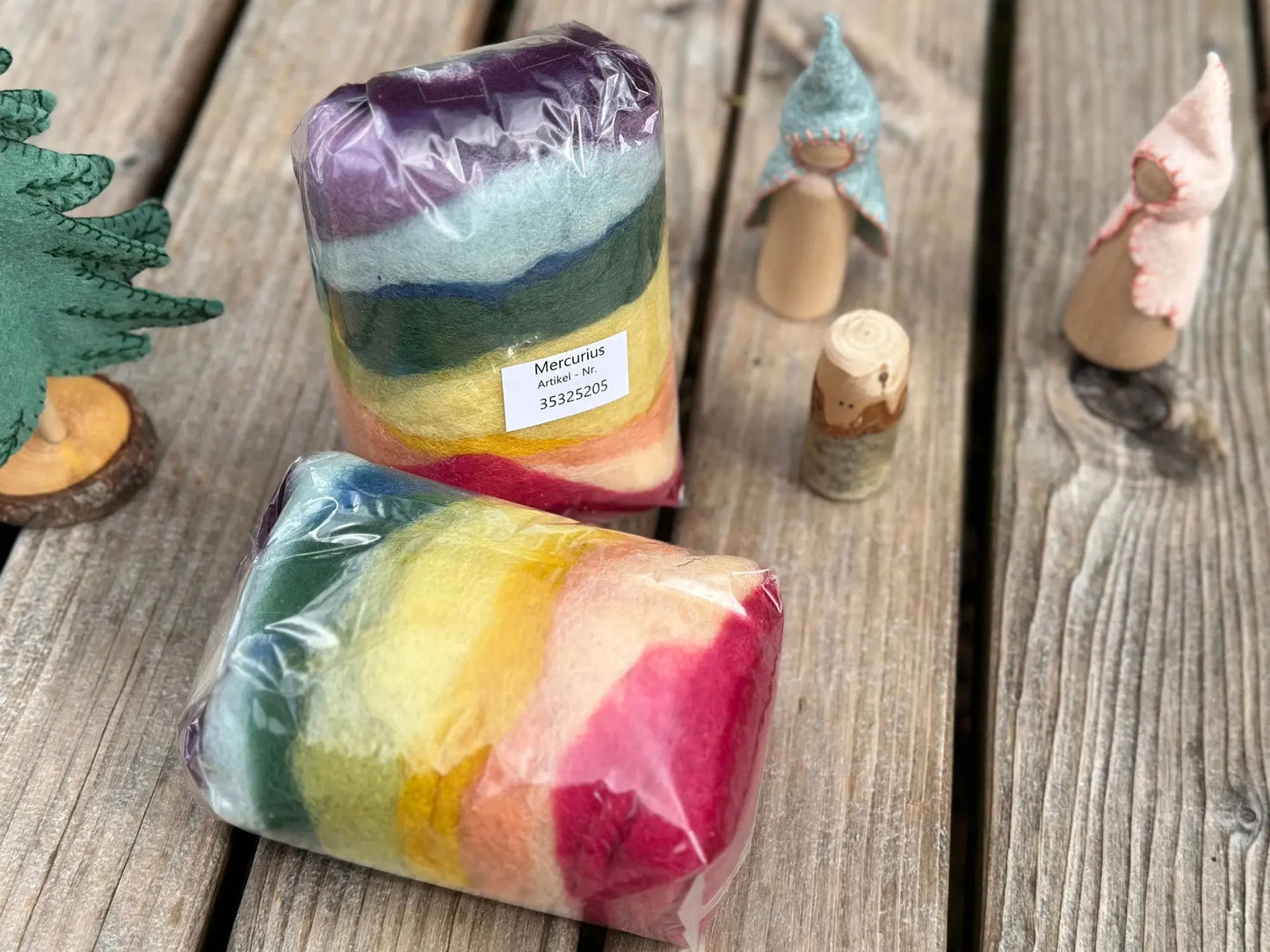 Two packages of colorful plant dyed wool on a wooden surface with figurines