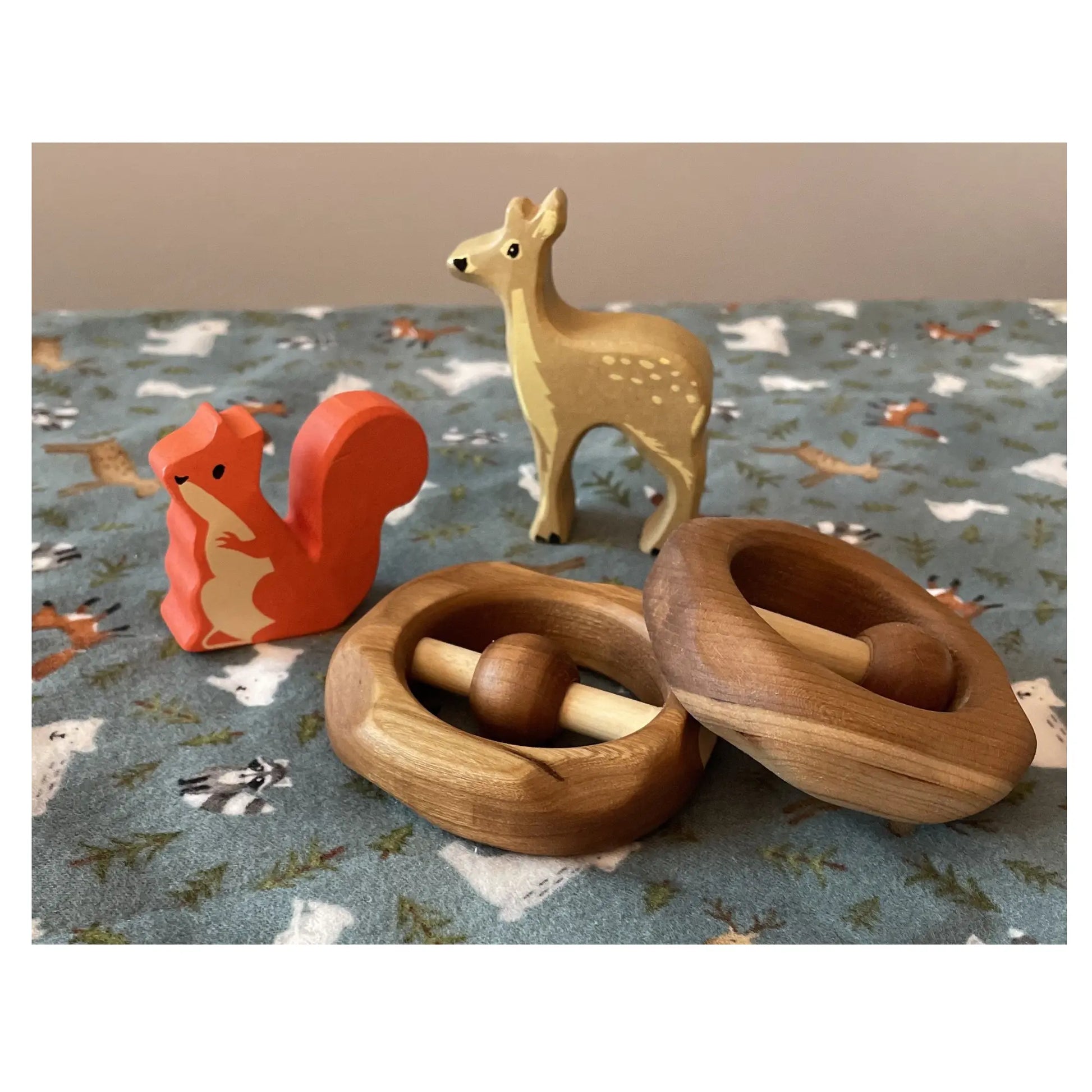 Wooden toys including a red squirrel, a deer, and two wooden cherrywood baby rattles on a patterned surface.