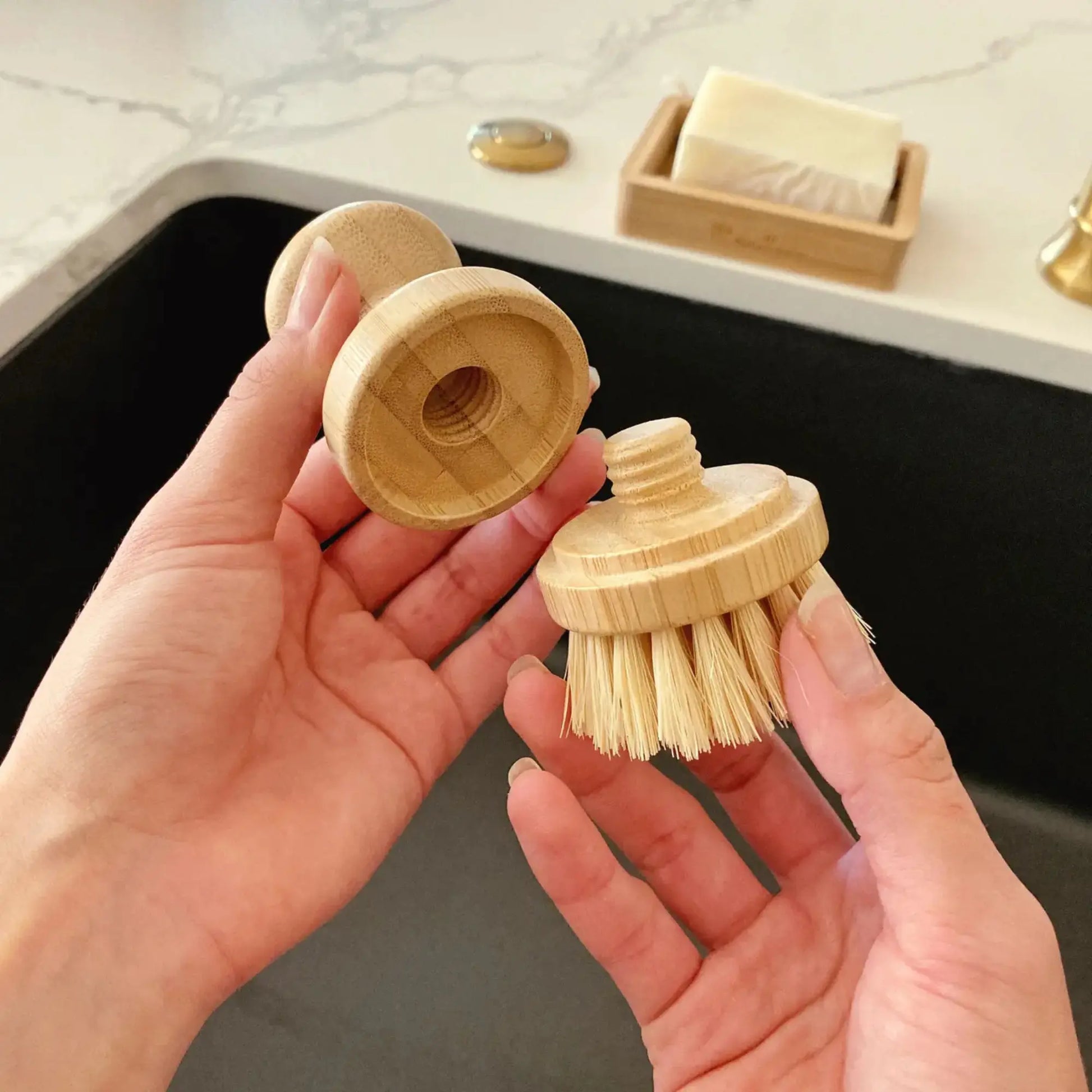 Wooden dish brush with detachable head held by hands in a kitchen setting.