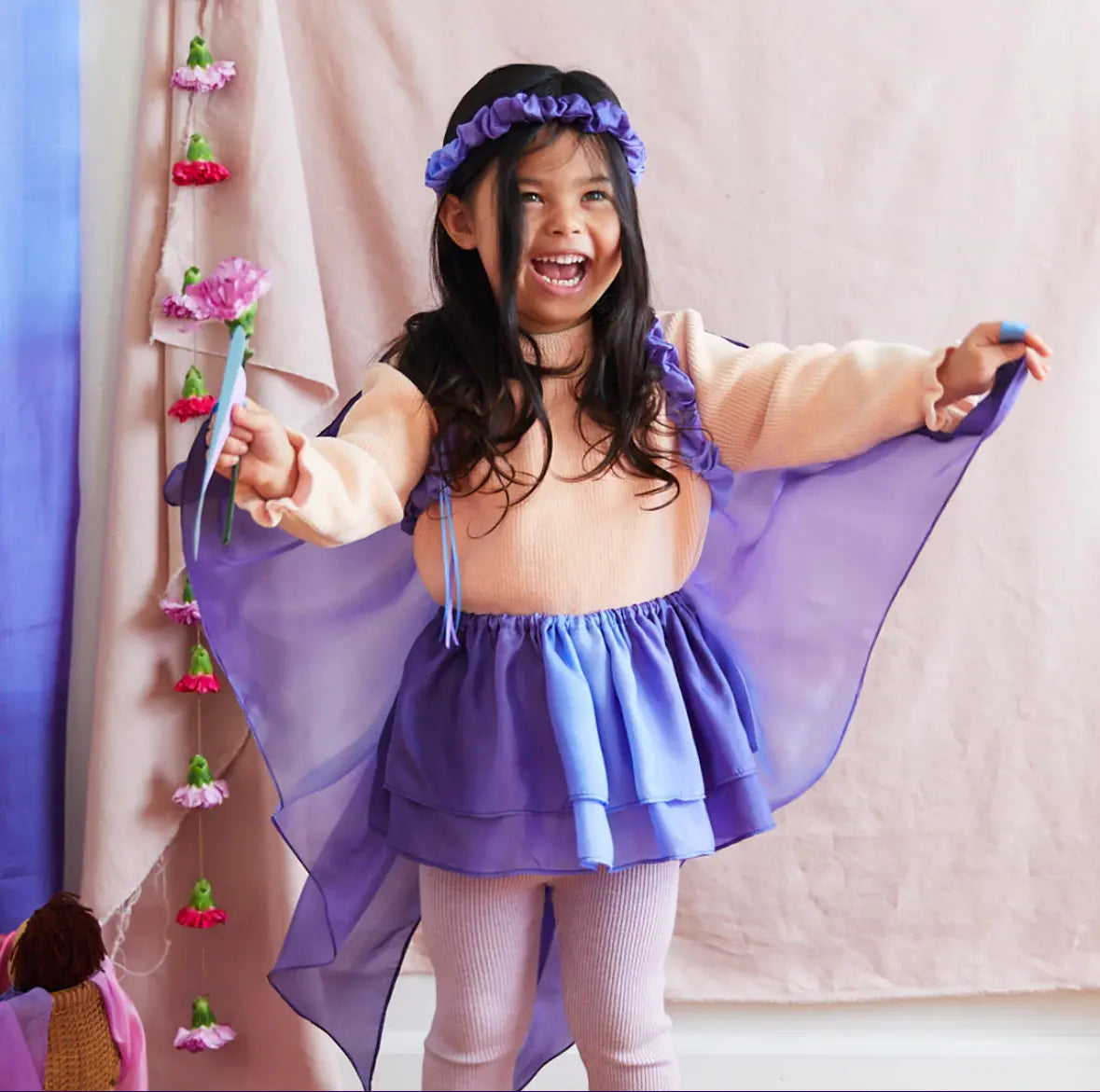 Child laughing joyfully in Butterfly Silk Tutu by Sarah’s Silks, holding flower.