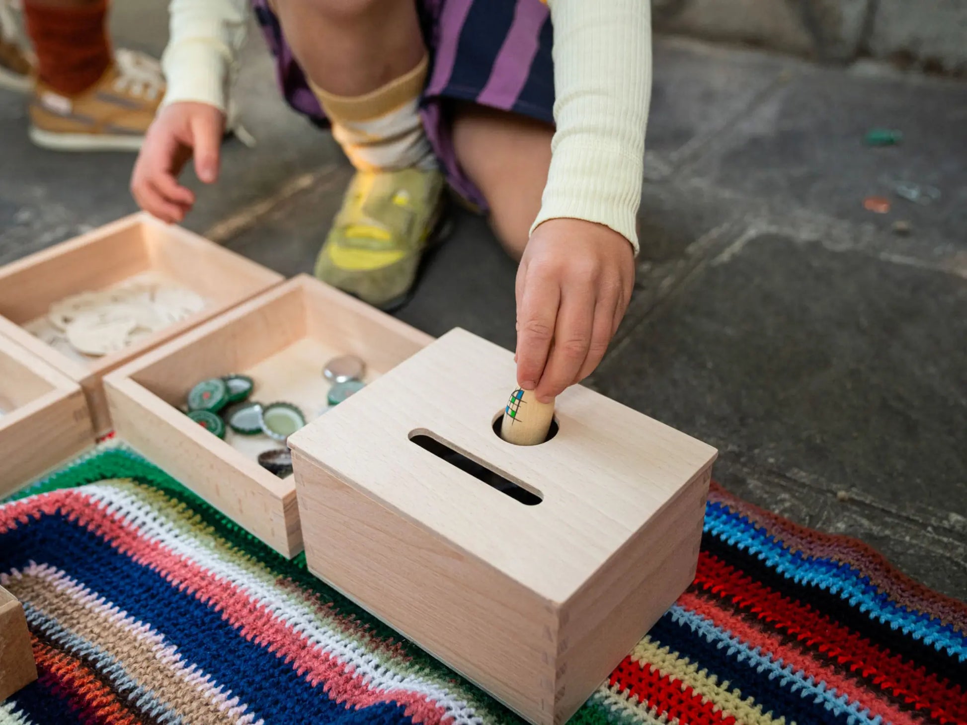 Child playing with a wooden treasure box on a colorful rug