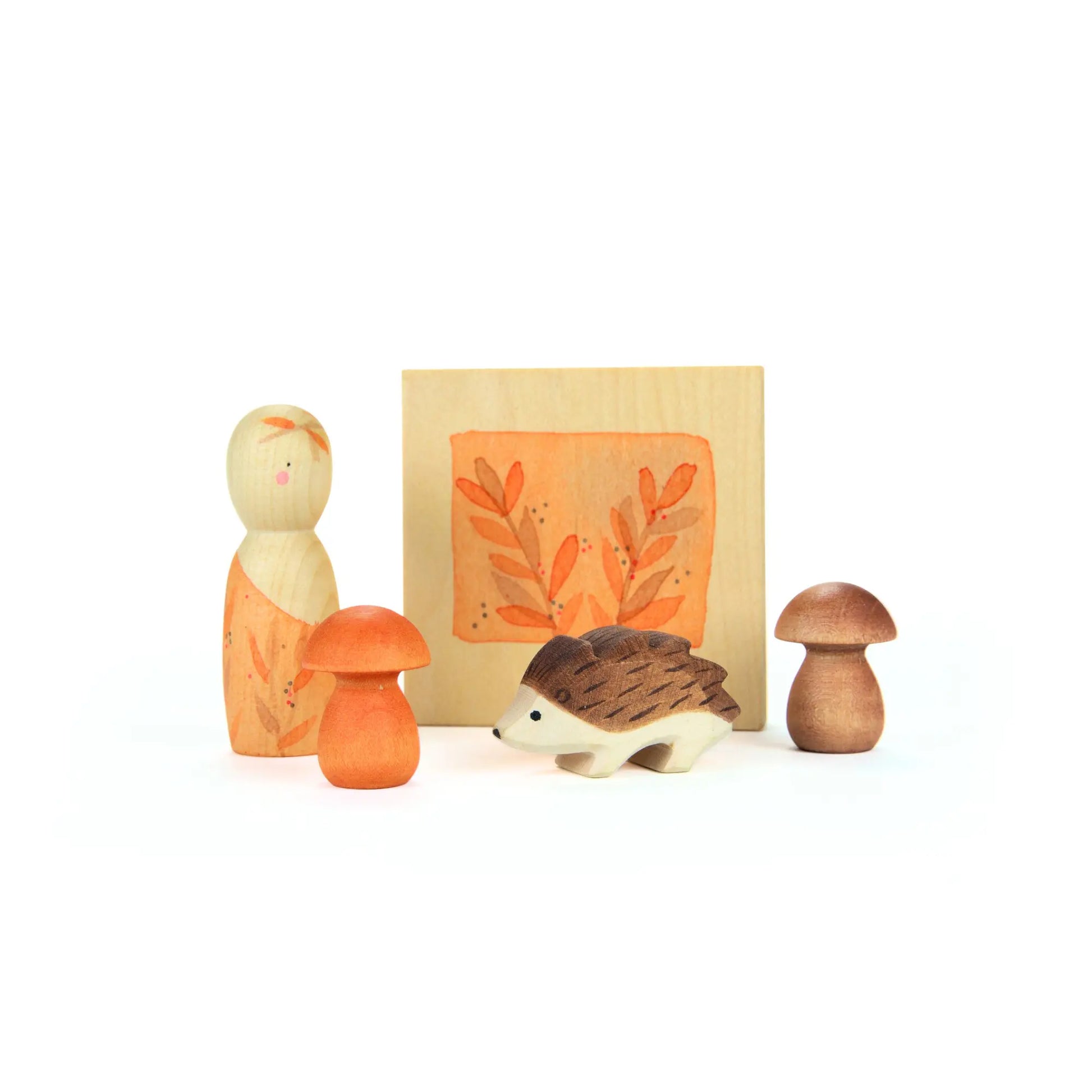 Waldorf wooden toys including a figurine, mushrooms, and a hedgehog in front of a wooden box with an illustration.